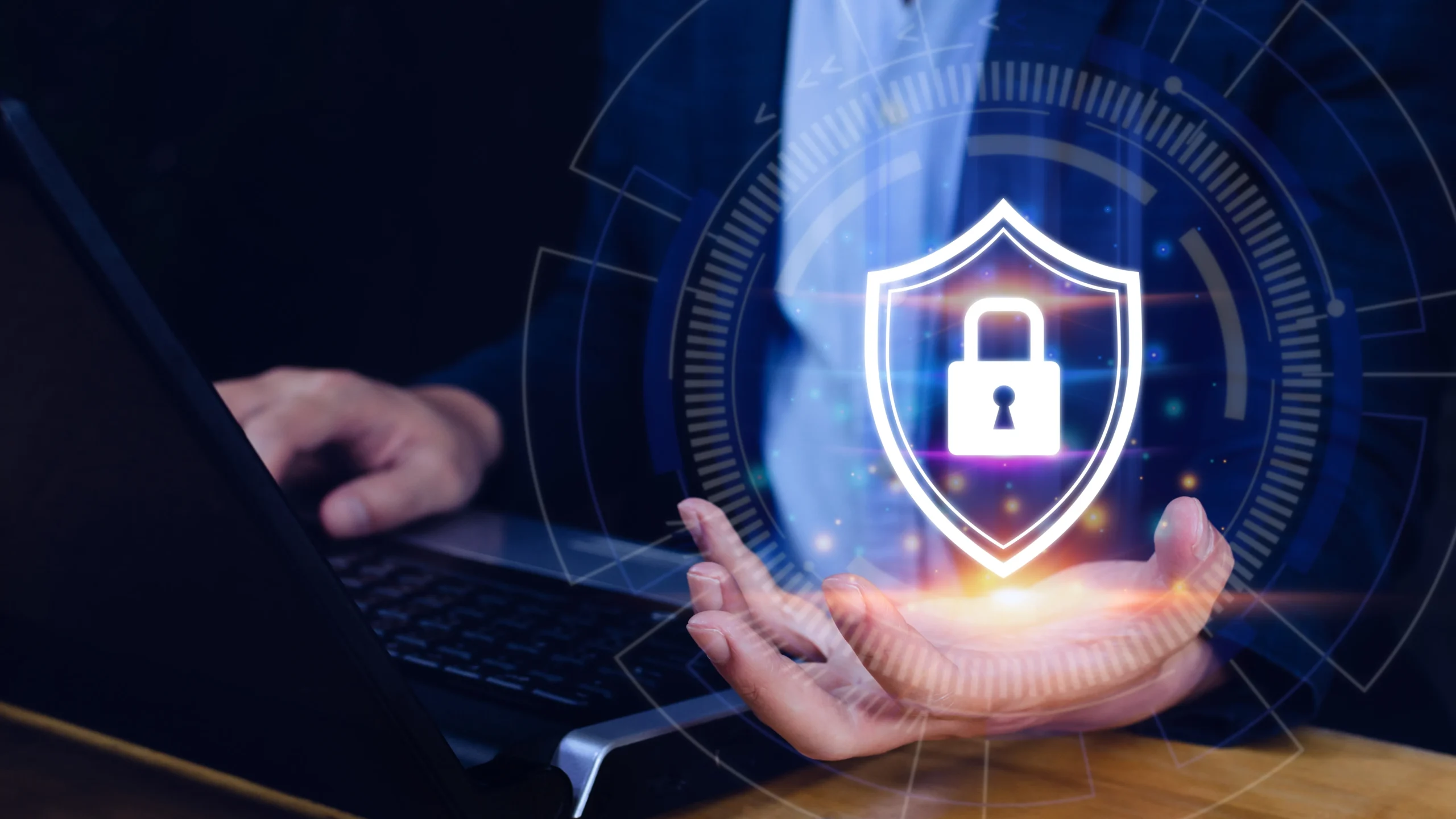 A person sits at a laptop with a glowing holographic shield and padlock above their hand, symbolizing cybersecurity and data protection. The tone is secure and futuristic.Data protection services, netsectechnologies
