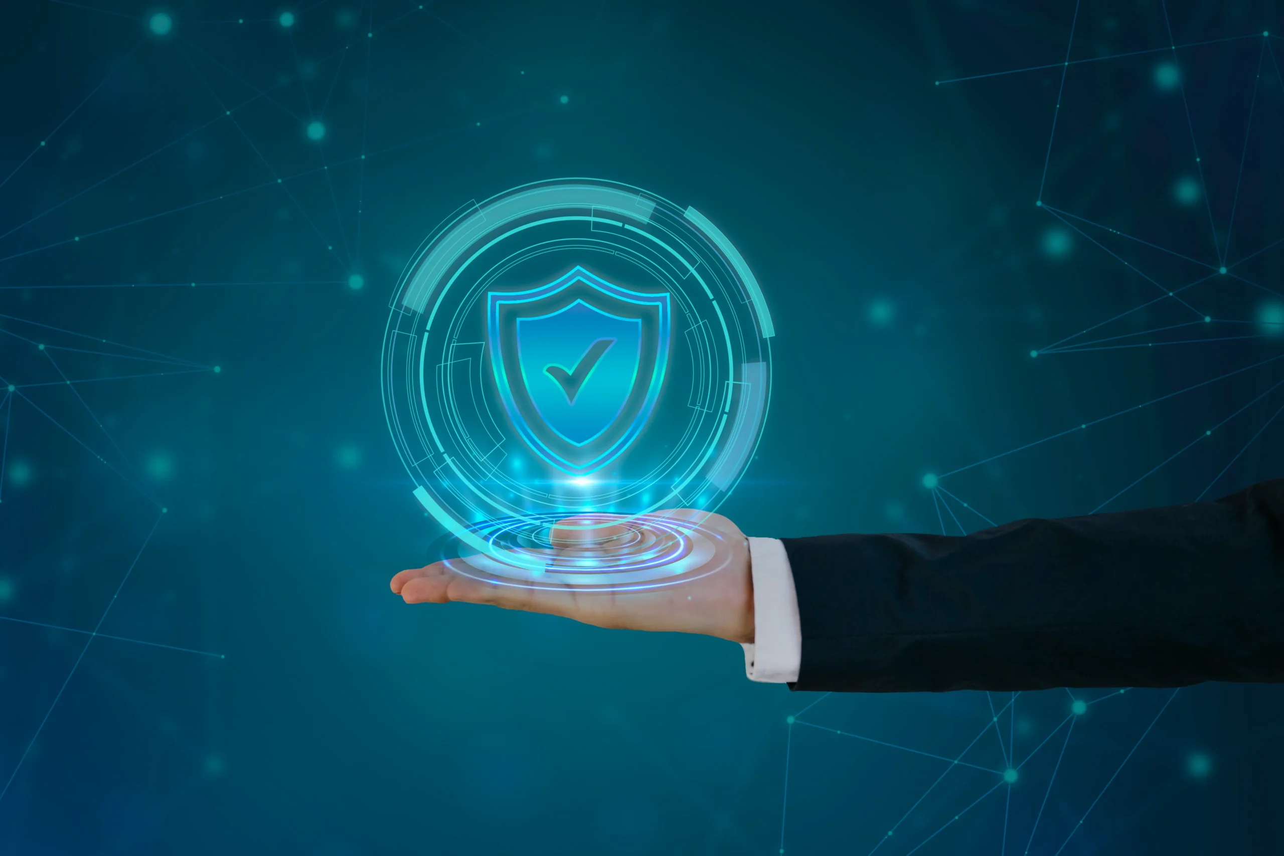 A hand in a suit presents a floating digital shield with a checkmark, symbolizing security. The blue background features connecting lines and glowing nodes.netsectechnologies