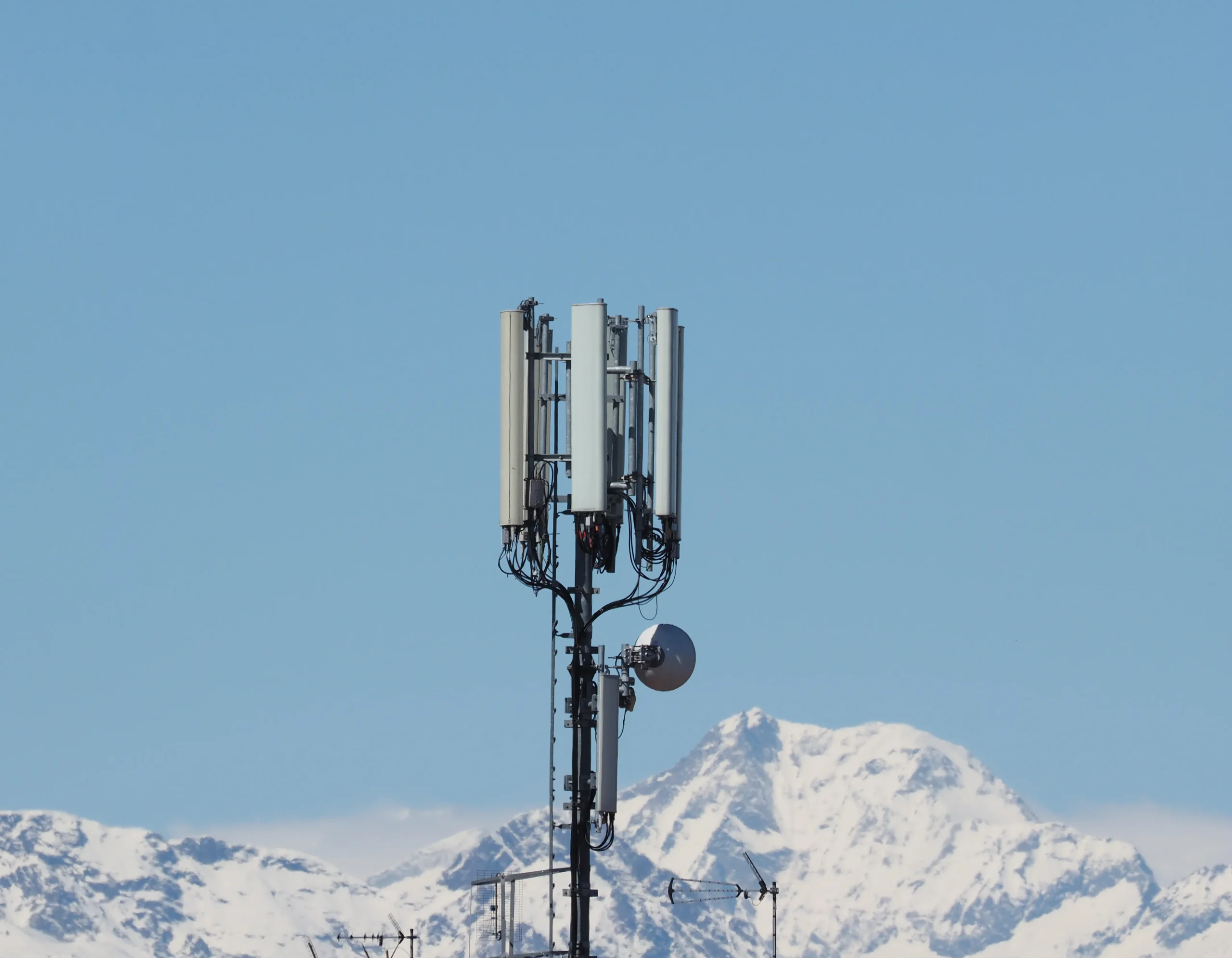 Cell tower stands tall against a clear blue sky with snow-capped mountains in the background, conveying a sense of technology amidst nature palo alto support with netsectechnologies
