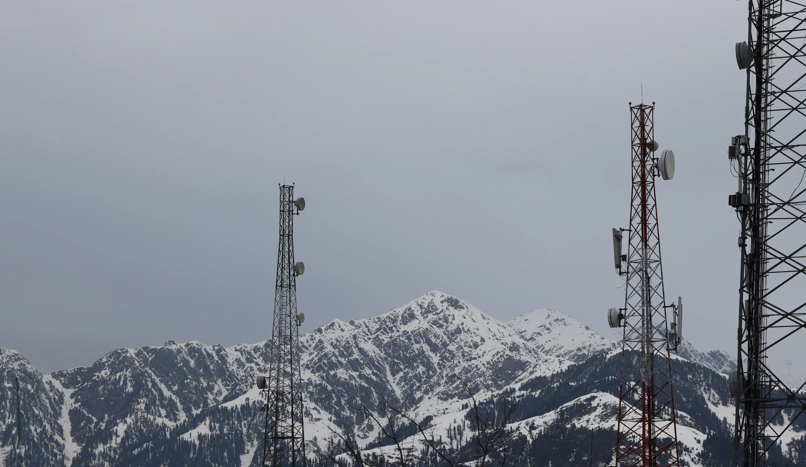 Cell towers stand before snow-covered mountains under a gray sky, creating a stark contrast between technology and rugged natural beauty palo alto support with netsectechnologies
